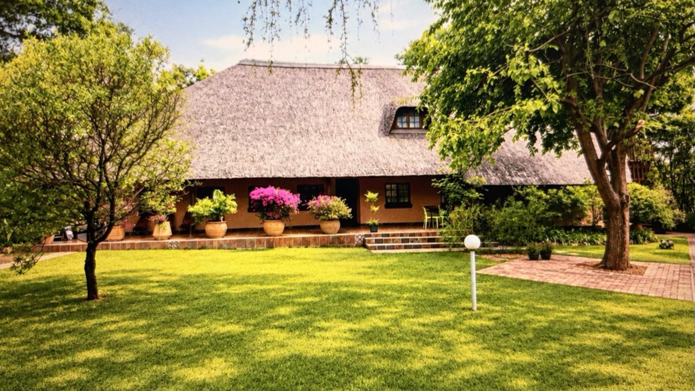 The thatched guest house seen across the lawn and established gardens